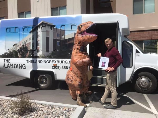 Photo of a guy in a t-rex costume and a guy with a piece of paper in front of the landing shuttle.
